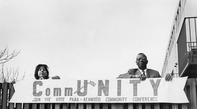 Black-and-white photograph of White woman and Black man holding sign that reads "CommUNITY. Join the Hyde Park-Kenwood Community Conference," circa 1960s.