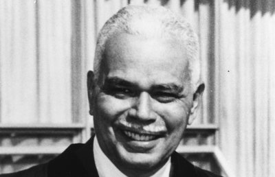 Black-and-white photograph of Allison Davis, the John Dewey Distinguished Service Professor of Education at the University of Chicago. Davis is shown wearing a dark suit and tie and smiling. He is a middle-aged African American man with short white hair and a white mustache.