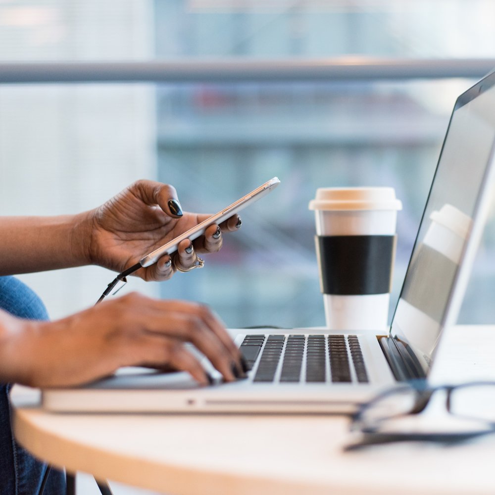 person on laptop holding a phone with a coffee nearby