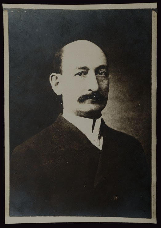 Bald man with mustache wearing high collar and no tie