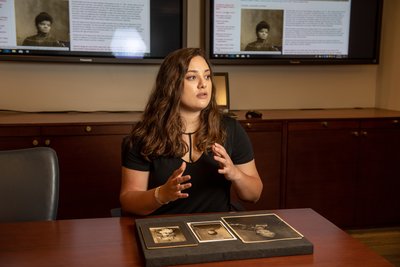 A Gray Fellow with archival photos in front of her and a related website behind her