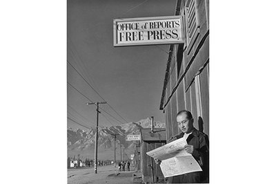 Black and white photograph of Editor Roy Takeno standing outside a newspaper office c. 1943