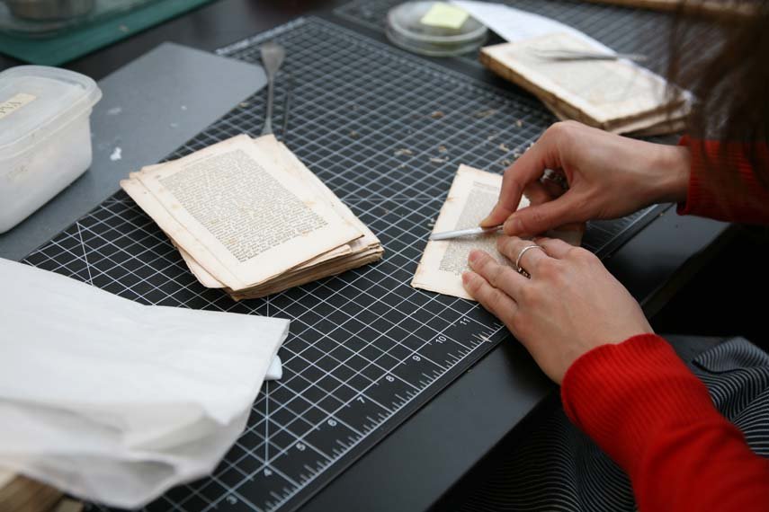 A conservator delicately pries off adhesive from the edge of a book page.