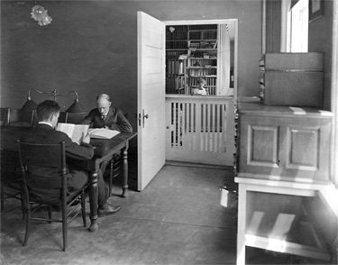 A room with two men studying at a desk.