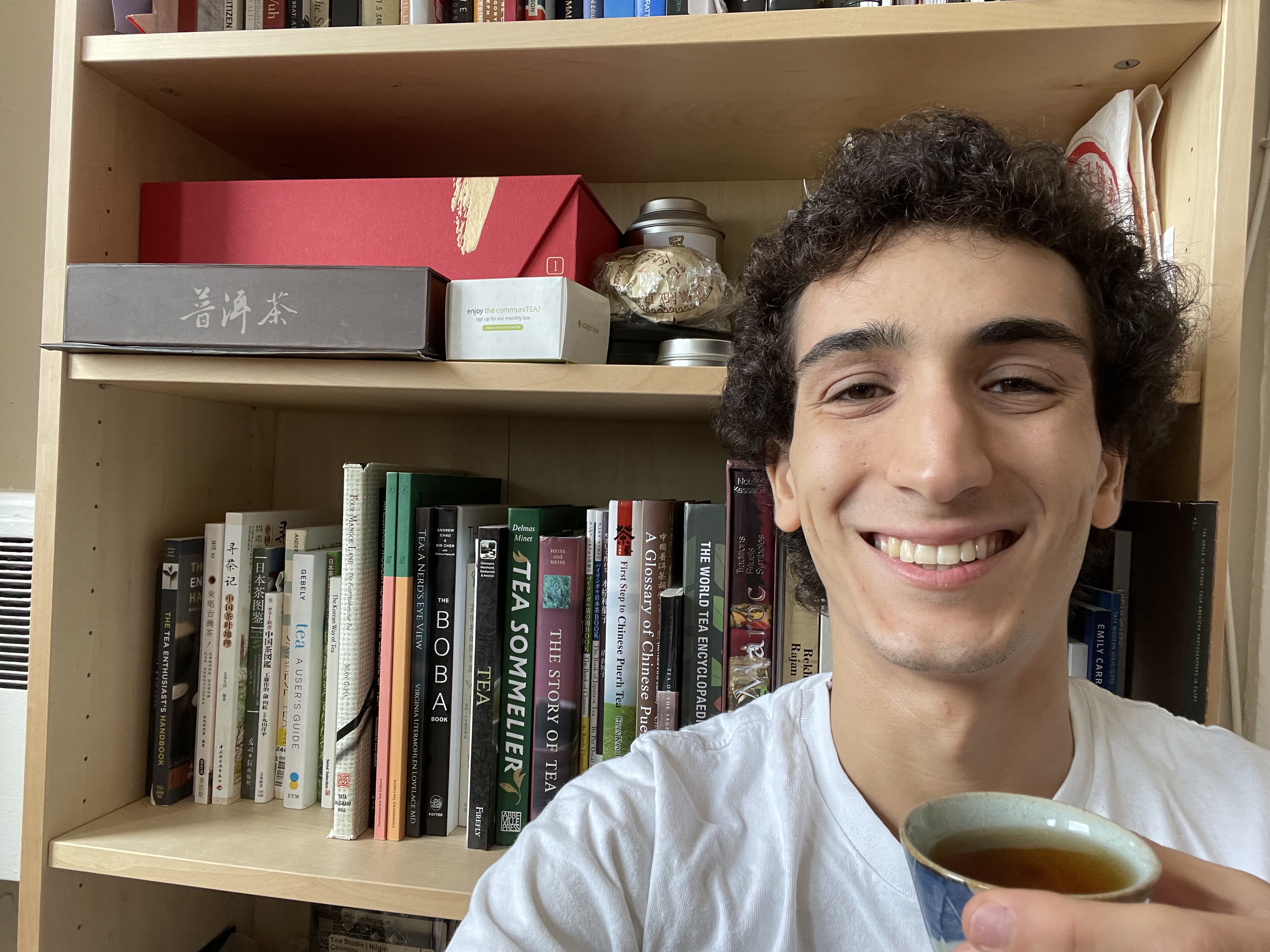 Portrait of Roberto Cohen. He is holding a cup of tea and sitting in front of a bookcase.