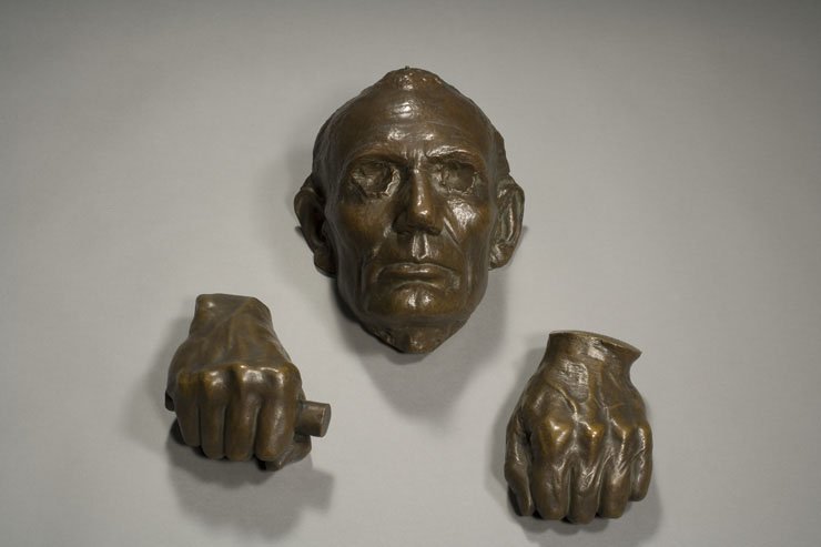 Metal casts of a man's face and closed hands.