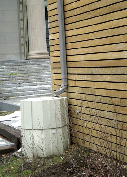 A white basin with a drainage pipe leading into it on the edge of a wooden building.
