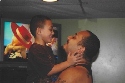 A child about 8 years old stands in front of an adult, who is looing up at the child, who is holding the adult's face. Toy Story is on TV screen in the background.