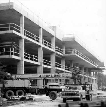 Trucks and construction equipment in front of a partially-finished building.