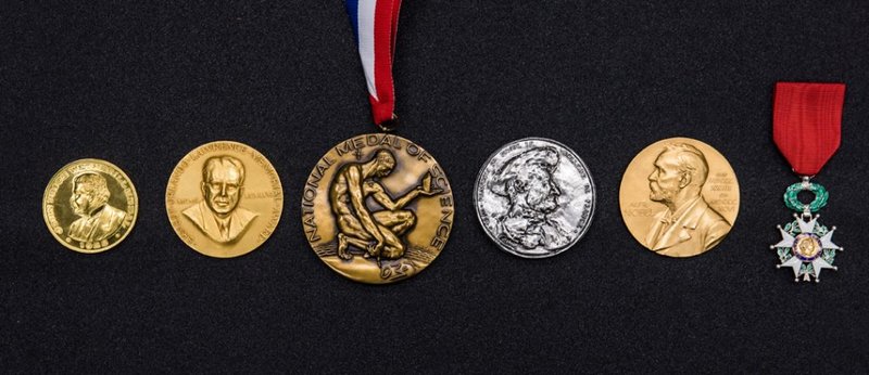 A row of silver and gold medals carved with various portraits of men.