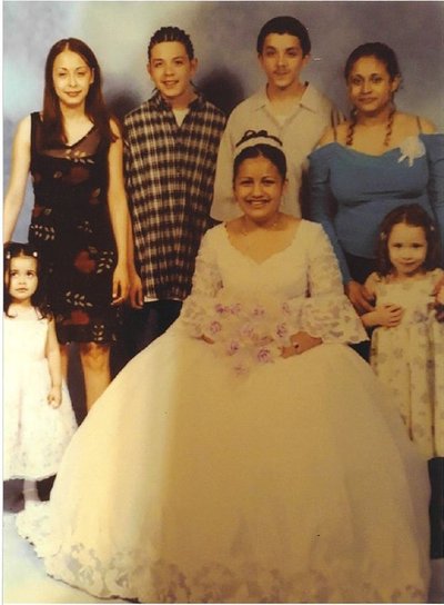 A family picture from a wedding, The bride is seated and surrounded by others: two young children, two teenagers and two adults.