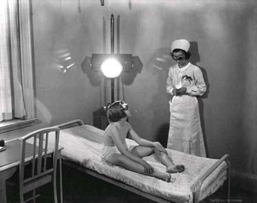 A nurse speaks to a boy sitting on a hospital bed; both wear dark goggles.
