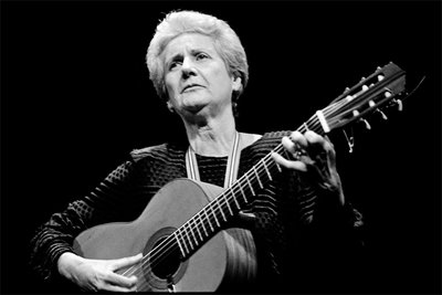 A black and white portrait of Giovanna Marini playing guitar.