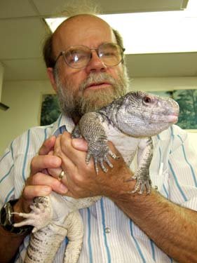 The same man, though much older, now  holds a large lizard.