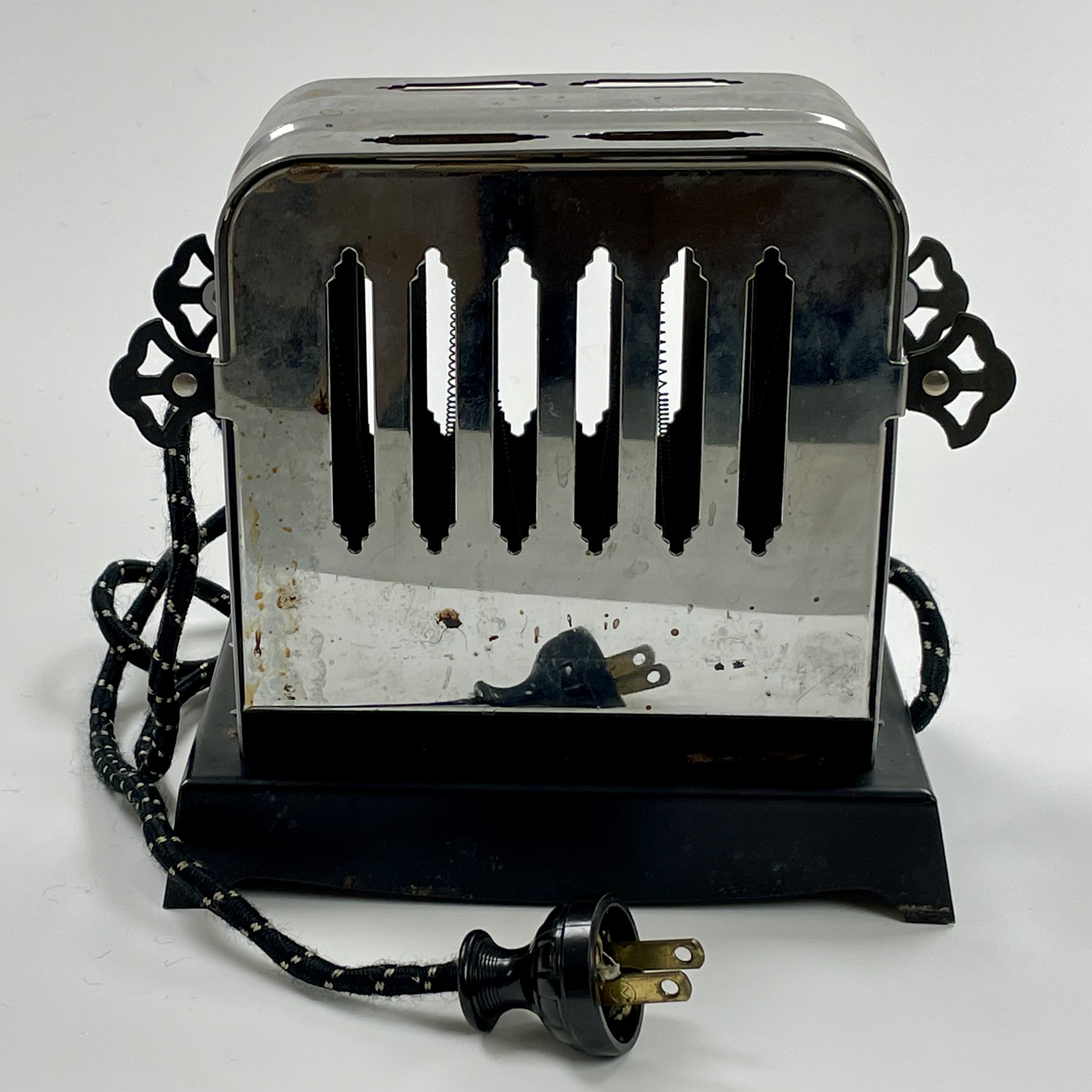 A silver electric toaster. There are slots on each side for the bread, and the cord and plug are coiled in front.
