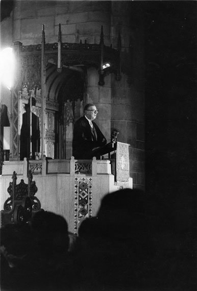 A man speaks at a podium in a Gothic building.