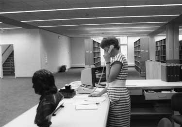 A woman at a reference desk answers the phone.