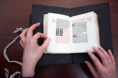 Hands hold open a book with text in red and black