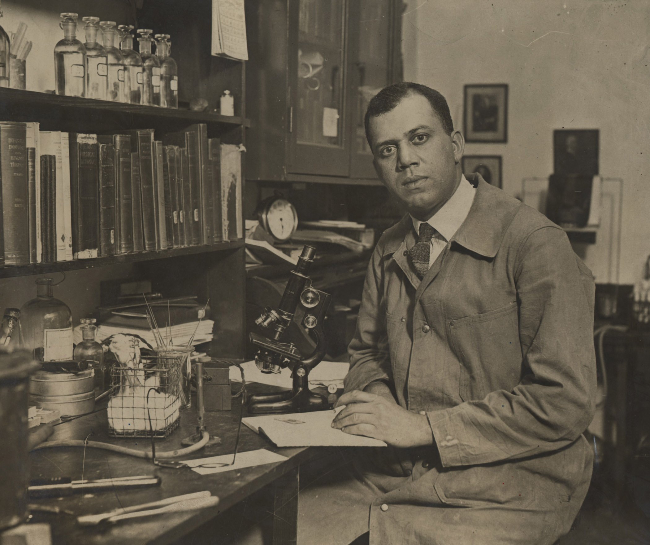Photograph of Dr. Julian Herman Lewis seated in front of a microscope in his lab.