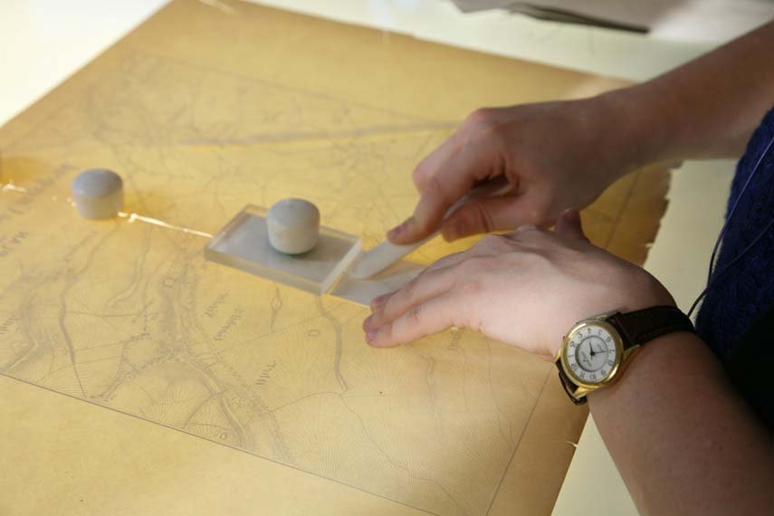 A conservator wields a delicate instrument over an old lit-up map.