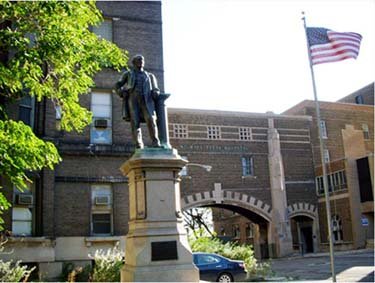 A modern brick building with a statue and an American flag in front.