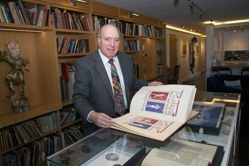Stephen Duchslag stands in front of bookcases holding a colorful Haggadah resting on top of a class case