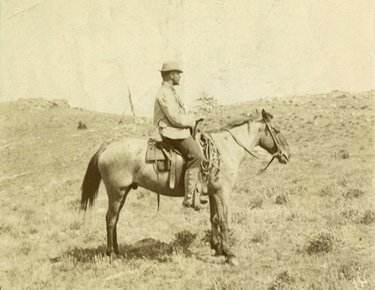 In an old photograph, a man sits astride a horse in the middle of the desert.