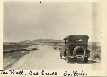An old car sits on a dirt road in a sparsely-populated plain.