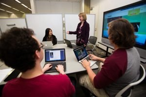 Librarian Rebecca Starkey with 3 students working on laptops.