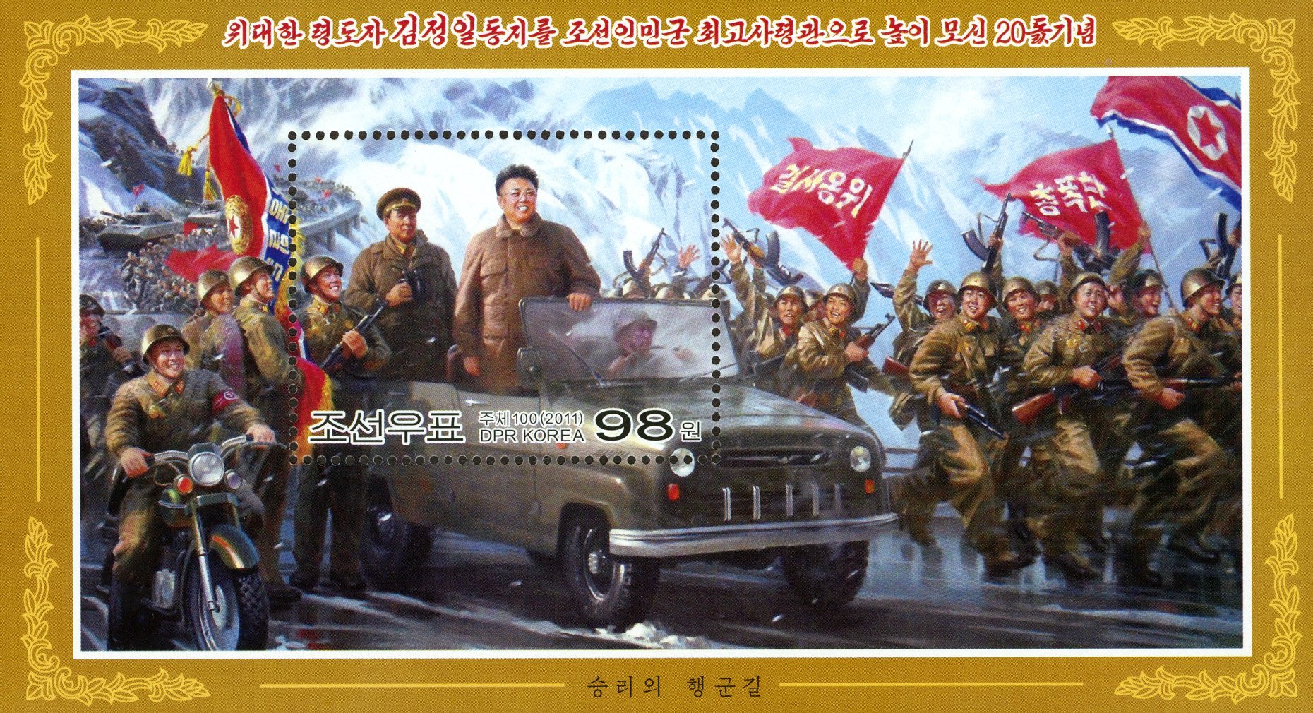 Kim Jong-il, with short black hair, glasses, and a brown suit, stands atop a moving truck while military men in fatigues, holding guns, celebrate and wave North Korean flags.