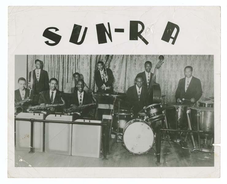 A group of musicians with saxophones, a drum set, and trumpets.