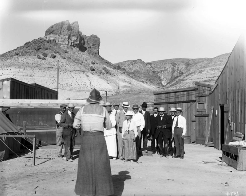 group of men and women in early 20th century garb pose for photo in western US landscape