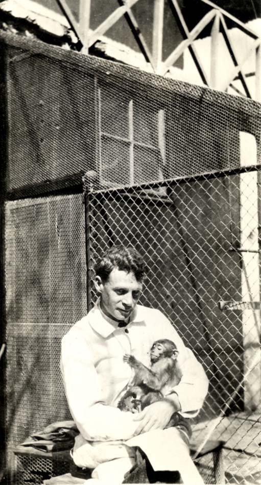 Man seated with small monkey cradled in his arms. The monkey looks comfortable.