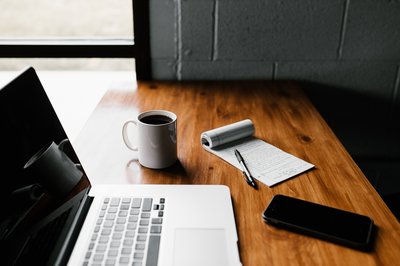 Computer, coffee cup, note pad and pen on table