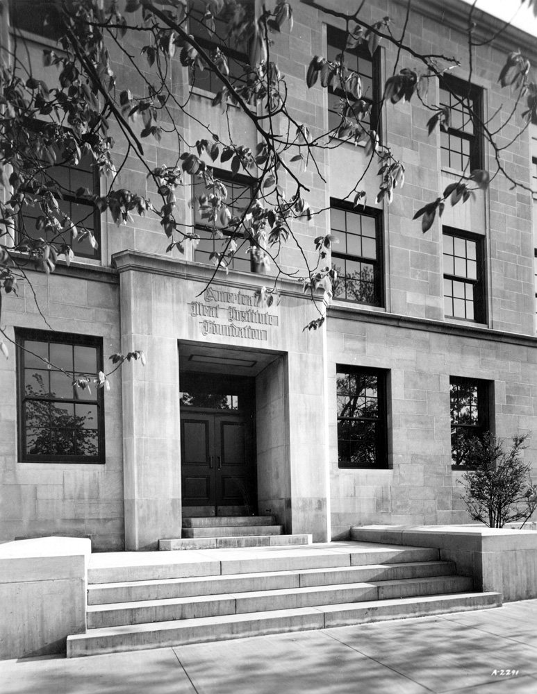 Black-and-white photograph of the exterior of the American Meat Institute building at the University of Chicago at 939 E. 57th Street. The building is stone, three-stories, has a wide four-step staircase leading to the central front door. Above the front door the words "American Meat Institute Foundation" are carved in Gothic script.