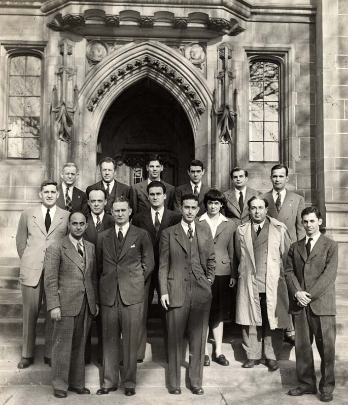 A black and white photo of a group of men and one woman who were the scientists working on CP-1, standing in front of a building on campus,