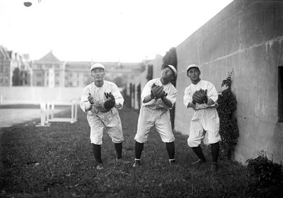 A black and white photograph of three baseball players posing for the camera. They are all pretending to field a fly ball, but are looking in different directions.