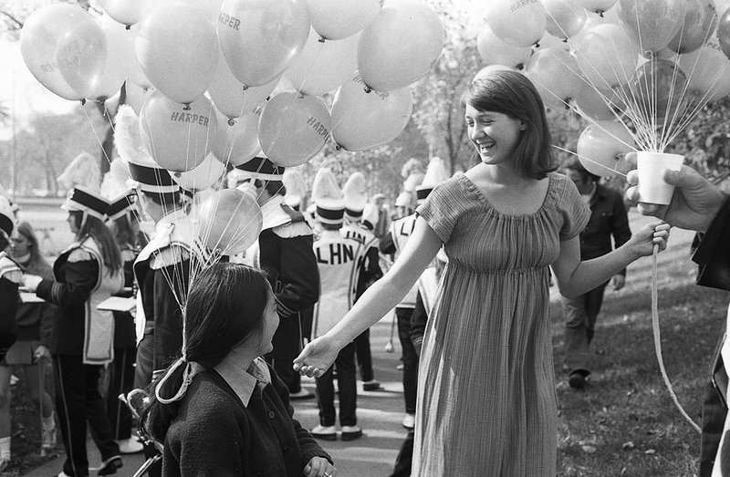 Two women shown against backdrop of white balloons and marching band