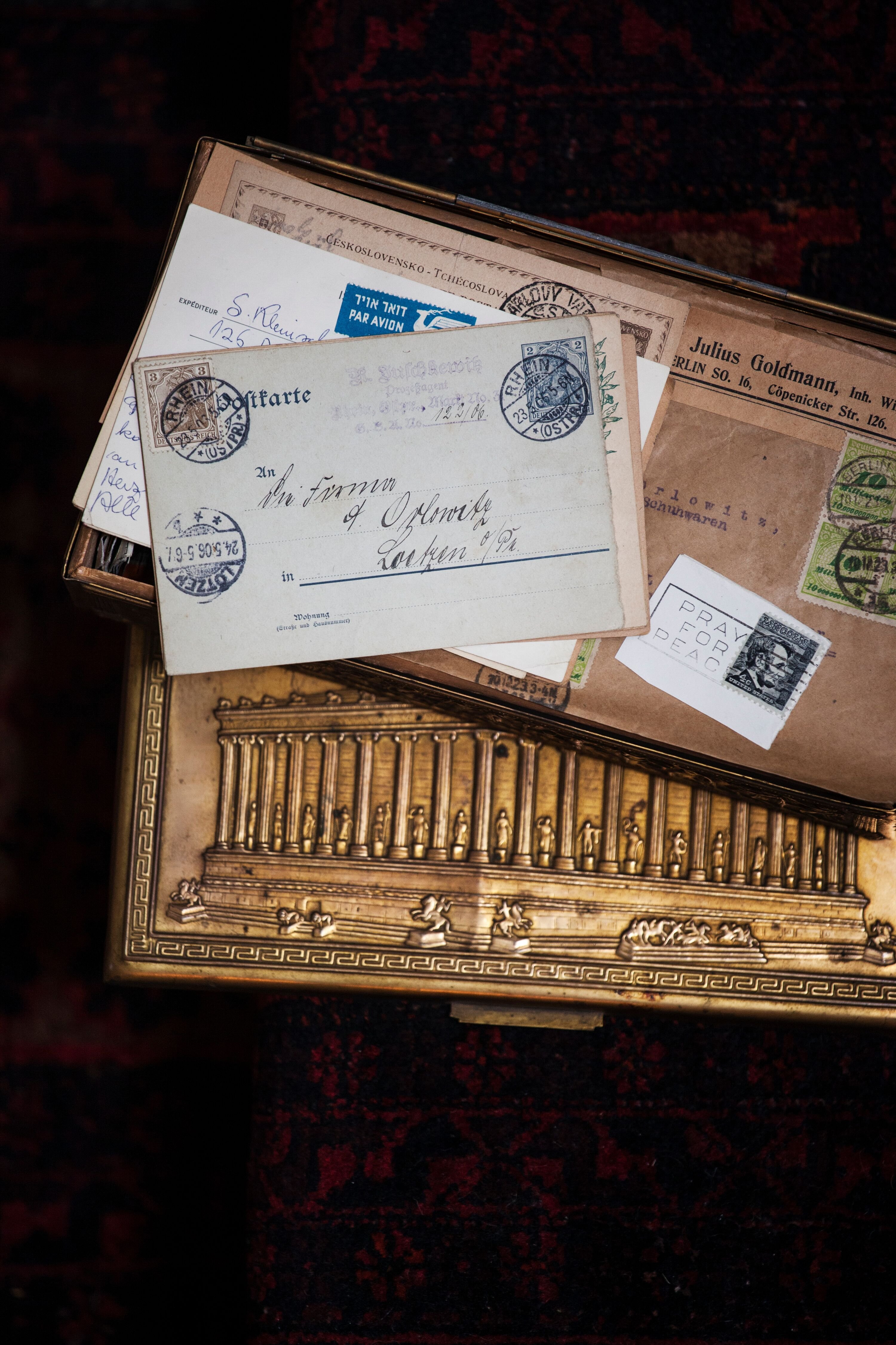 A gold metal box with a carving of the Parthenon, and several letters and packages on top.