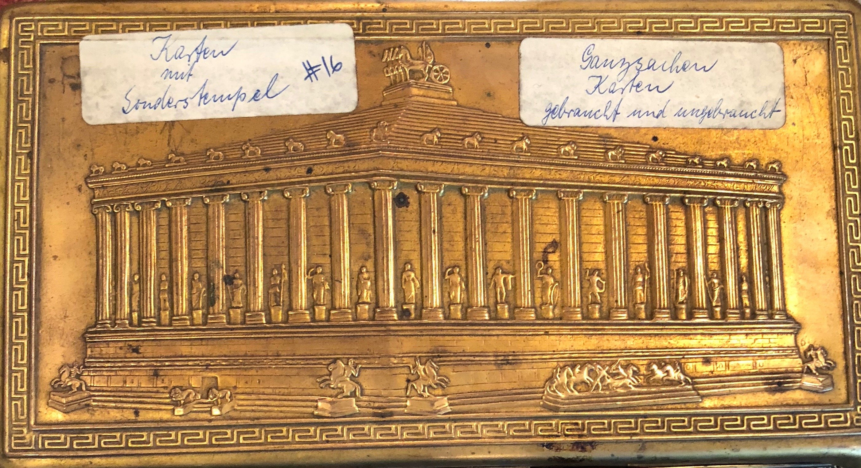 A gold metal box with a carving of the Parthenon and a German label.