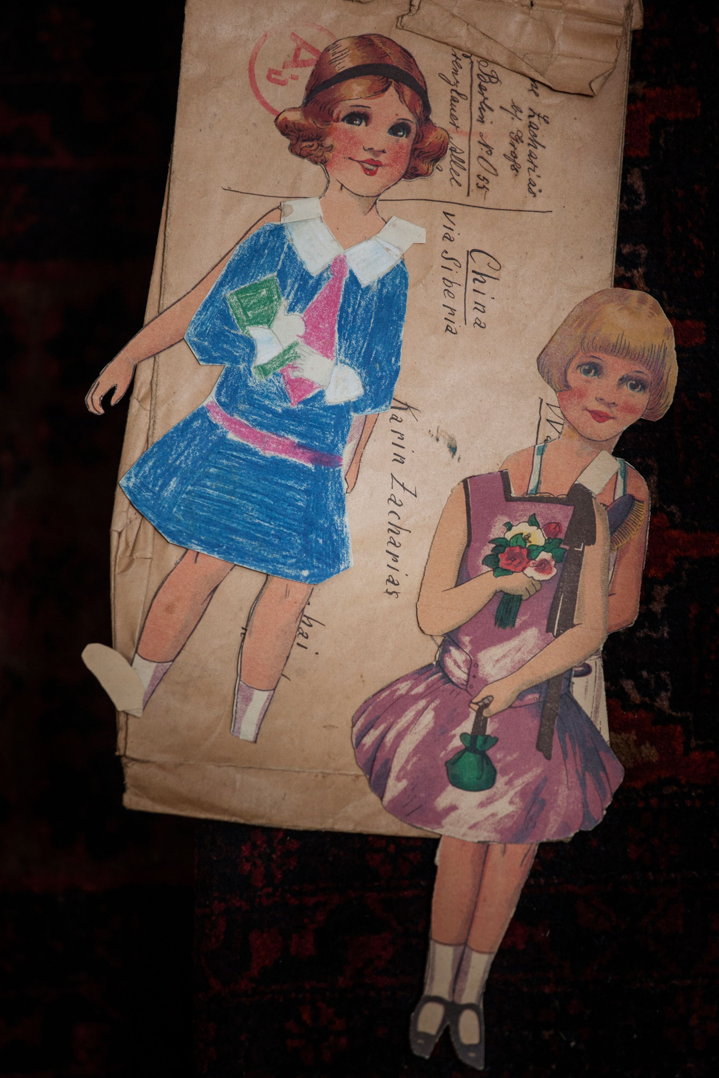 Cut-outs of two paper dolls with colorful dresses, holding books and flowers.