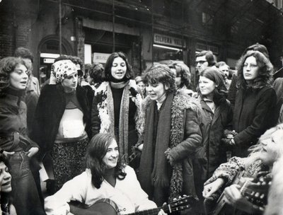 A group of women standing around a seated woman with a guitar.