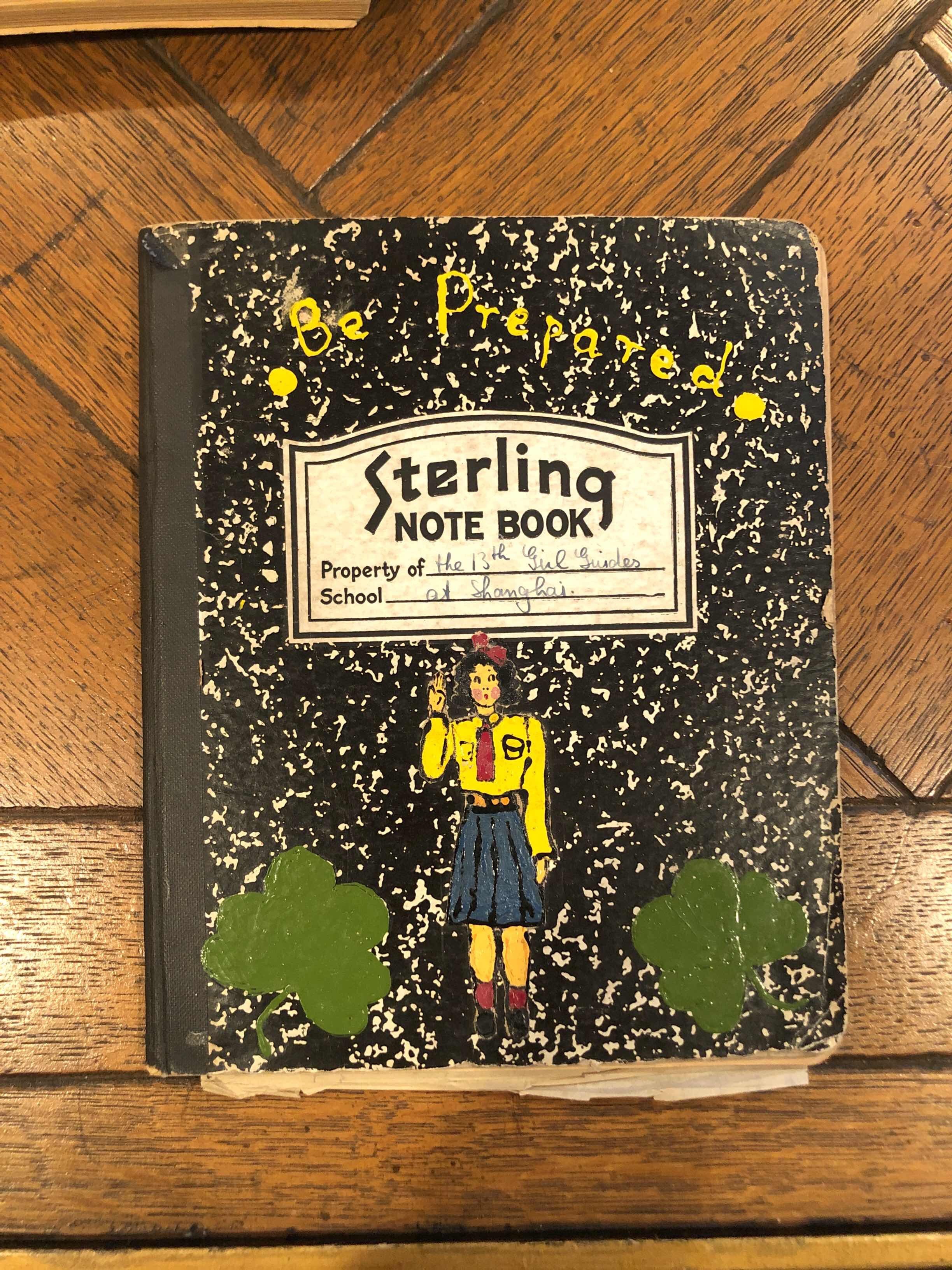 A composition notebook with the front illustration of a girl wearing a yellow-and-blue uniform; the notebook says "Be Prepared."