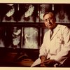 Photography of Dr. Kirsner, MD, PhD standing in front of gastrointestinal-related x-rays. Photographer and date unknown.