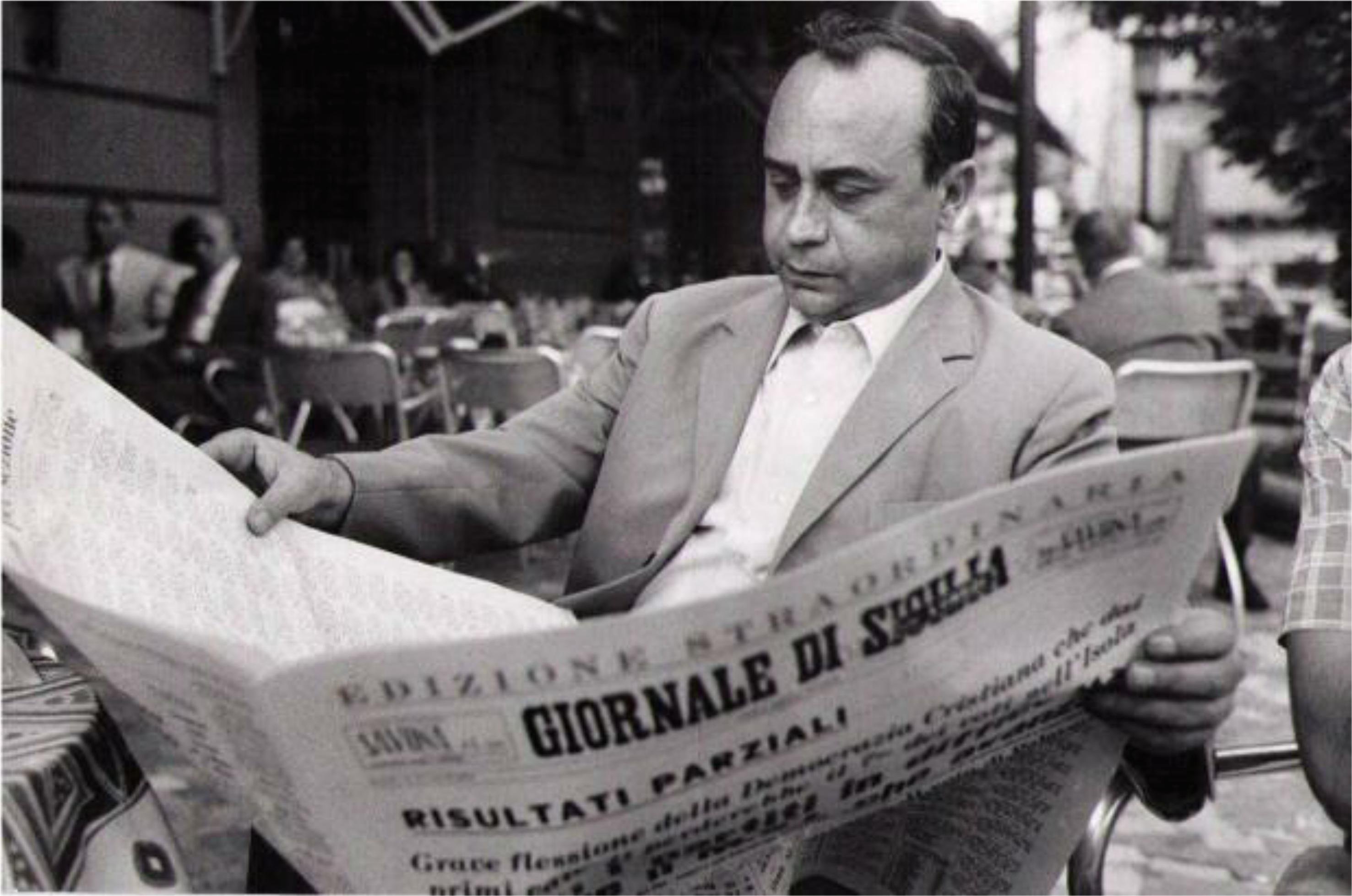 A black and white portrait of Leonardo Sciascia, reading a newspaper outdoors.