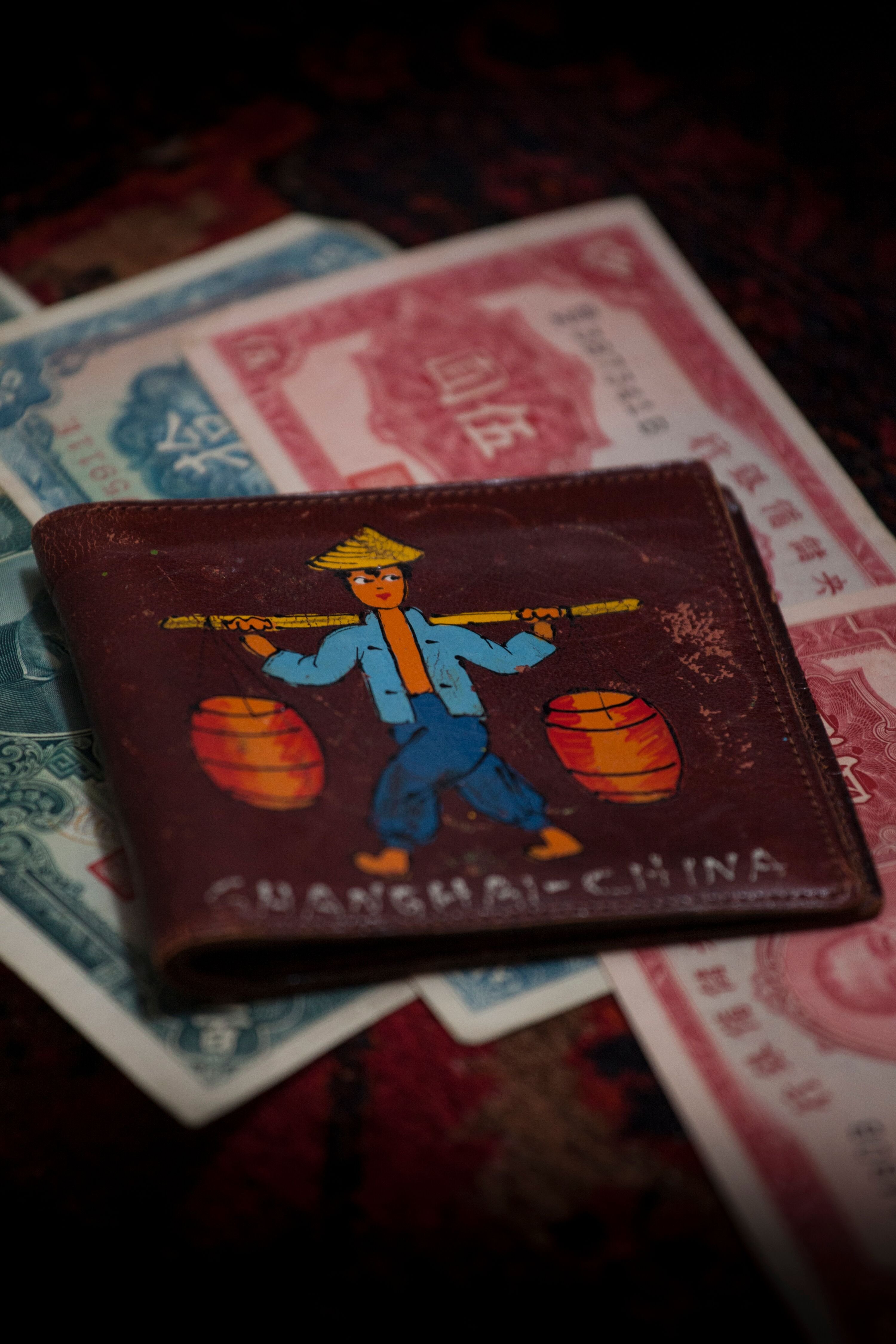 A brown wallet decorated with the painting of a man holding buckets hanging from a rod balanced on his shoulders.