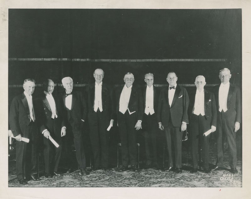 Black-and-white group photograph of nine older white men wearing tuxedos.