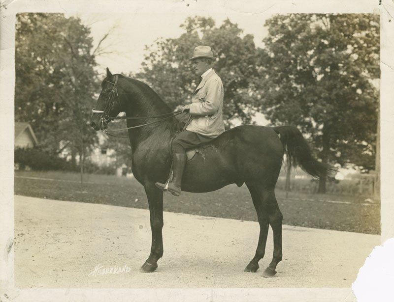 Black-and-white photograph of Thomas E. Wilson riding saddle horse "Kentucky Choice." Kentucky Choice is a dark horse and is shown in profile. Thomas E. Wilson is a middle-aged white man wearing a light-colored riding suit and hat.