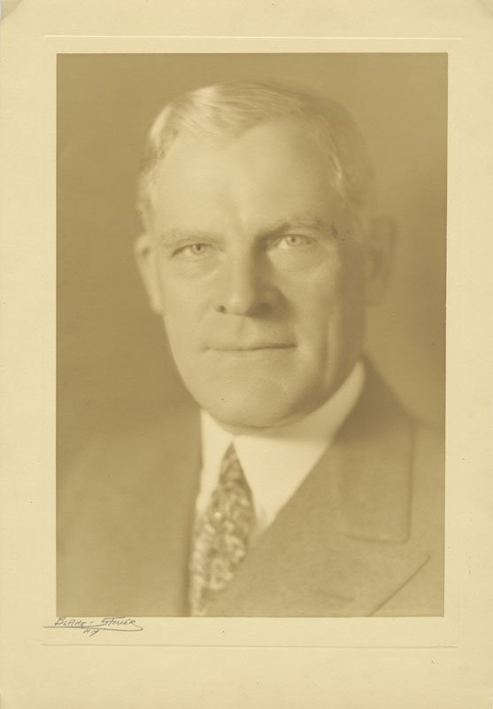 Black-and-white formal photographic portrait of Thomas E. Wilson. Thomas is a middle-aged white man, is wearing a suit and tie, has short white hair, and is looking directly into the camera. The portrait is cropped from the shoulders up.