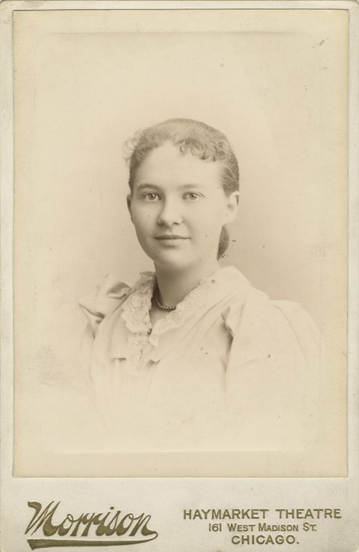 Black-and-white formal photographic portrait of Elizabeth Foss Wilson as a young girl. She is a young white woman shown from the shoulders up, wearing a light colored dress with short dark hair tied in a bow at the nape of her neck. She is looking straight into the camera with a slight smile.